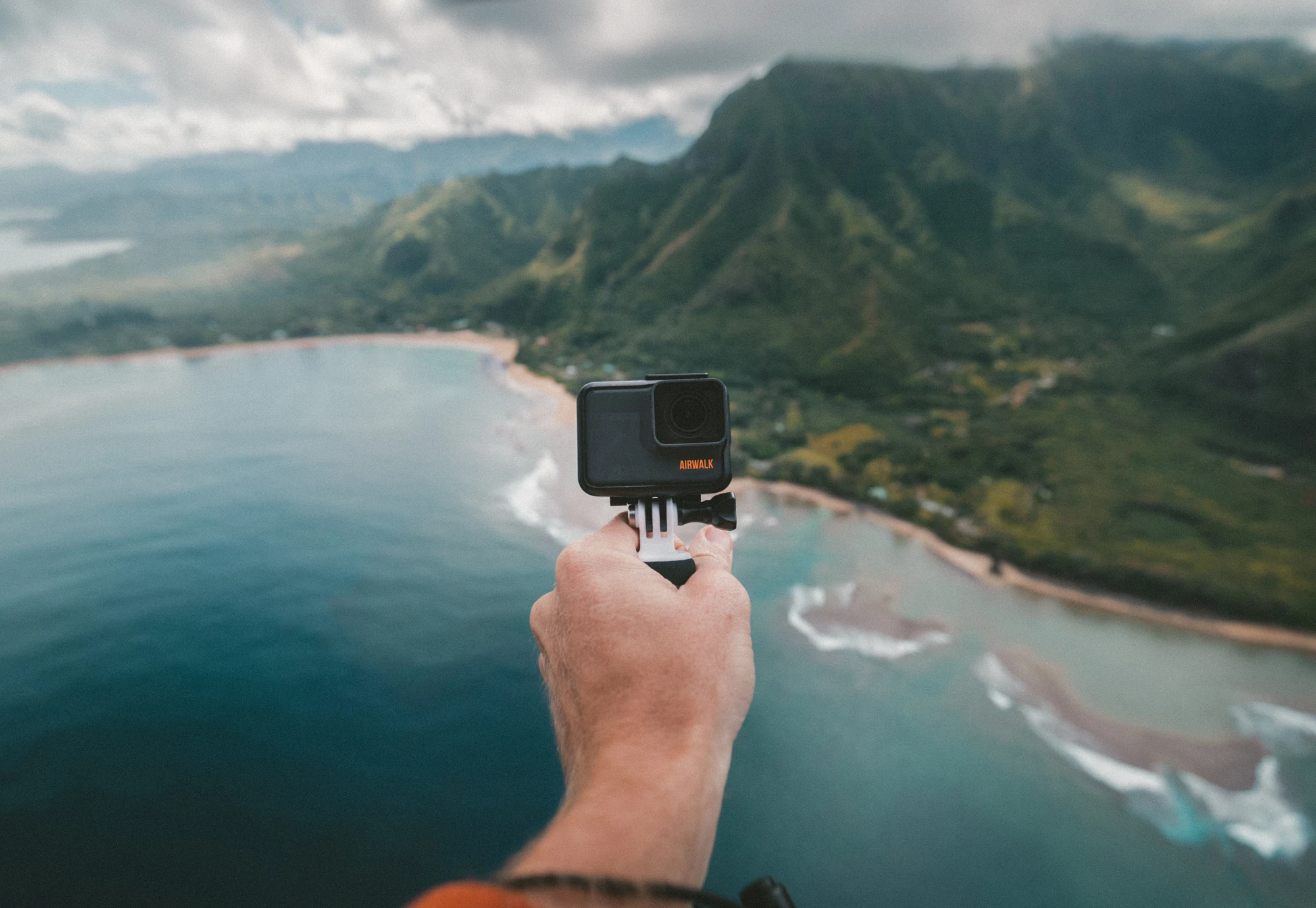 Hand holding an action camera above a coastal landscape